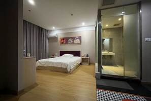 Una habitación de hotel moderna con cama, mesita de noche y zona de ducha con paredes de cristal.