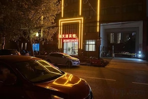 A street scene at night with cars parked along the curb and a building with illuminated signage.