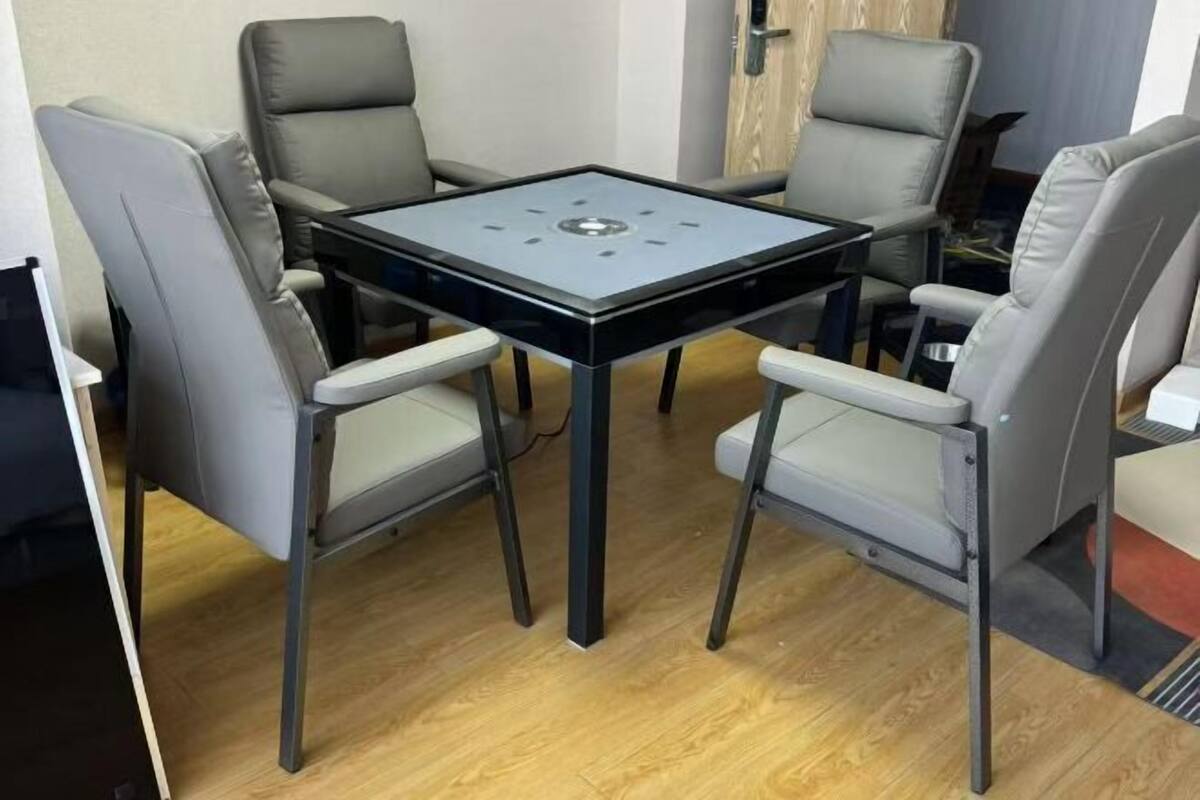 A small, square table with a black top and four grey chairs with light grey cushions.