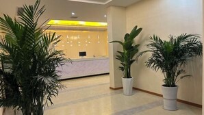 A hotel reception area with a marble counter, potted plants, and a tiled floor. - Zhongxiangshun Tianyuan Business Hotel (Zhongxiang)