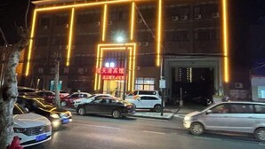 A building with illuminated neon lights outlining its structure, parked cars, and a red sign with Chinese characters. - Zhongxiangshun Tianyuan Business Hotel (Zhongxiang)