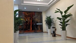 A hotel lobby with a modern design, featuring a glass door entrance, potted plants, and a chandelier. - Zhongxiangshun Tianyuan Business Hotel (Zhongxiang)