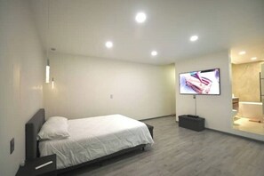 Ein modernes Hotelzimmer mit einem Bett, einem flachbildfernseher an der Wand und einer kleinen Sitzecke mit Tisch und Stuhl.