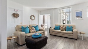 Un salón amplio con dos sofás color beige, un reposapiés marrón y una mesita redonda pequeña.
