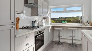 Una cocina moderna con armarios blancos, una estufa a gas y una ventana con vistas a la vegetación.