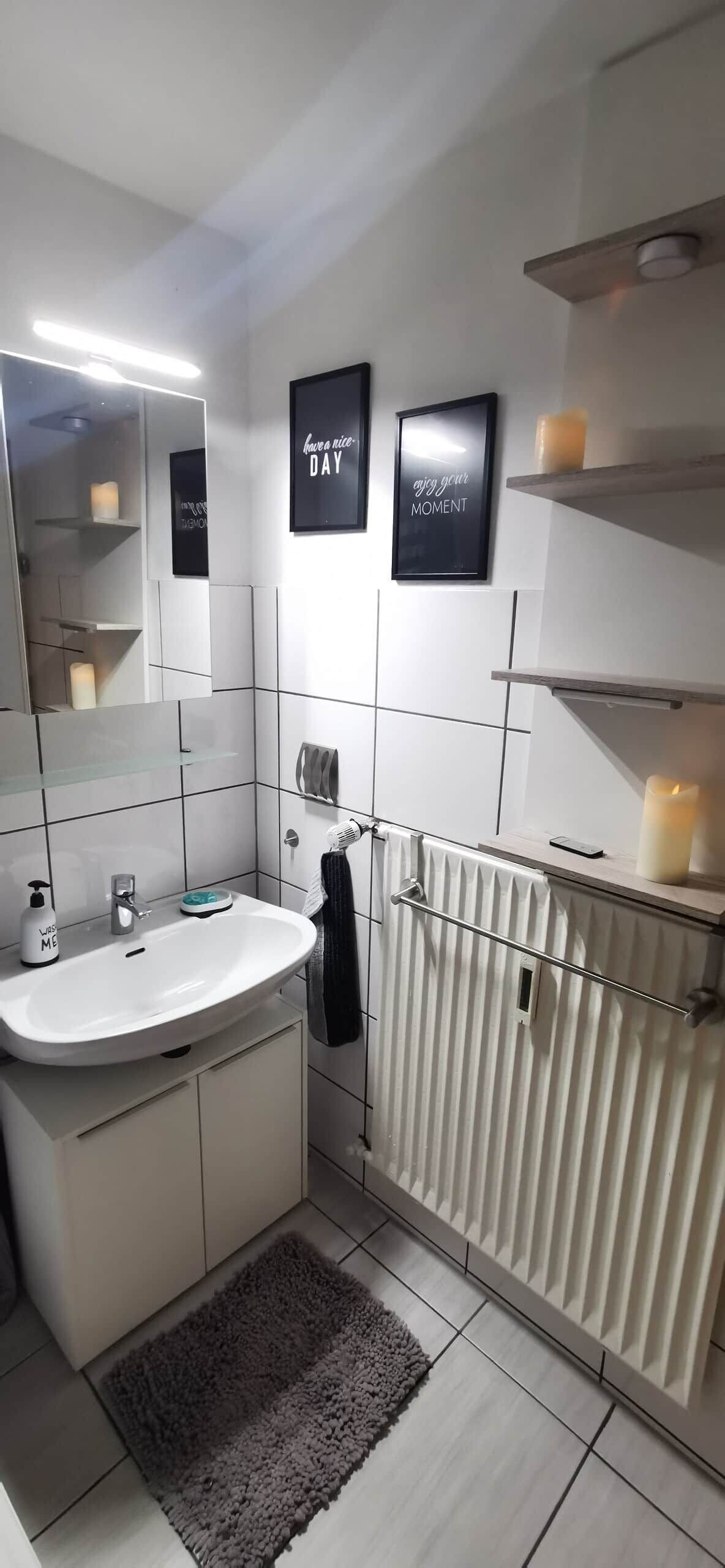 A modern bathroom with a white sink, mirror, and a towel rack. There are two framed motivational posters on the wall.