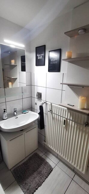 A modern bathroom with a white sink, mirror, and a towel rack. There are two framed motivational posters on the wall.