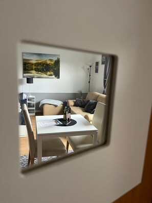 Uma sala de estar moderna com um sofá branco, uma mesinha com uma garrafa e uma figura decorativa, um abajur e um quadro na parede.