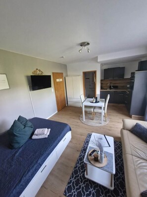 A modern apartment with a bed, a sofa, a dining table, and a kitchen area.