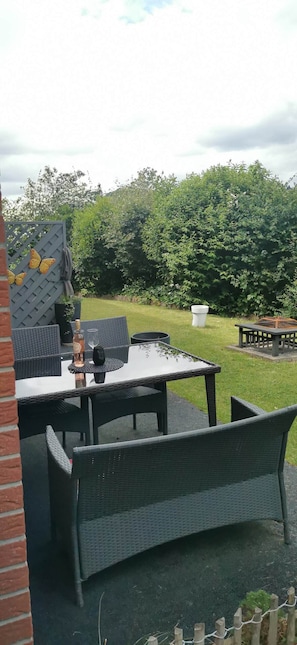 An outdoor patio with a table and chairs, a decorative fence, and a garden in the background.