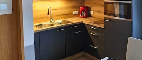 A modern kitchen with dark cabinets, a stainless steel range hood, and a built-in oven.