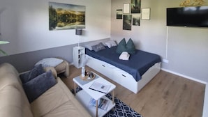 A modern living room with a sofa, a bed, a flat-screen TV, and a ceiling fan.