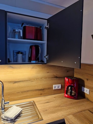 Eine Küche mit einer Holzauslage, einer roten Kaffeemaschine und einem Schrank voller Küchenutensilien.