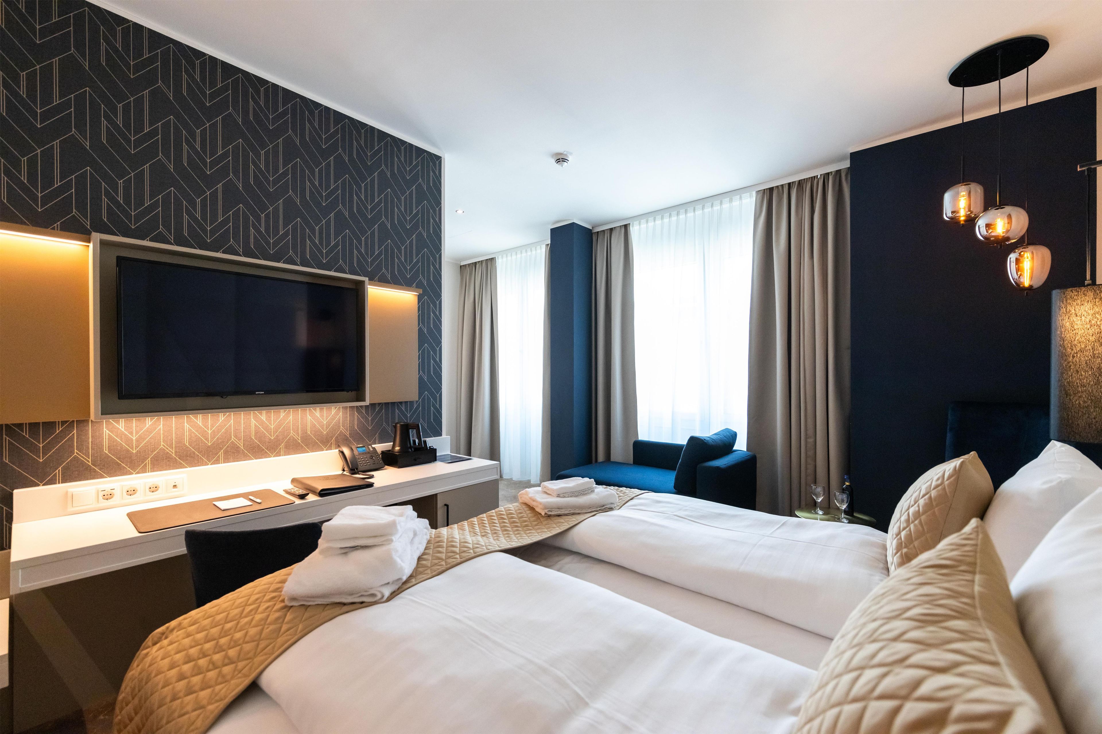 A hotel room with a bed, bedside table, TV, and a window with curtains.