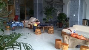A spacious living area with a round wooden table, sofas, and potted plants. - Dali Shuanglang Caiyunjian Inn (Dali City)