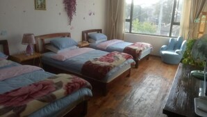 A room with three beds, a wooden floor, a window with curtains, a chair, and a desk with a fan. - Dali Shuanglang Caiyunjian Inn (Dali City)