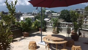 A rooftop terrace with a round table and chairs, surrounded by potted plants. - Dali Shuanglang Caiyunjian Inn (Dali City)
