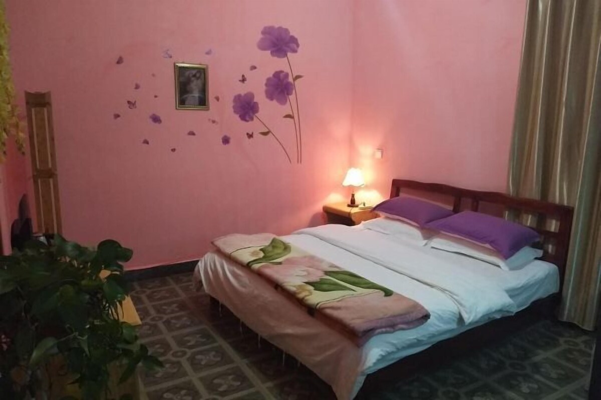 A bedroom with a bed, a nightstand, a lamp, a wall decoration, and a plant.