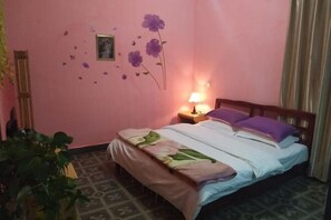 A bedroom with a bed, a nightstand, a lamp, a wall decoration, and a plant. - Dali Shuanglang Caiyunjian Inn (Dali City)