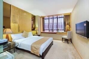 A hotel room with a bed, bedside tables, a TV, a window with curtains, and a desk with a chair.