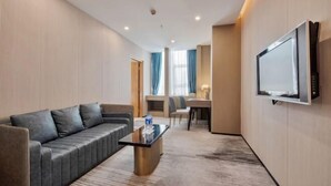 Et hotelværelse med sofa, sofabord, fjernsyn og skrivebord med stol.