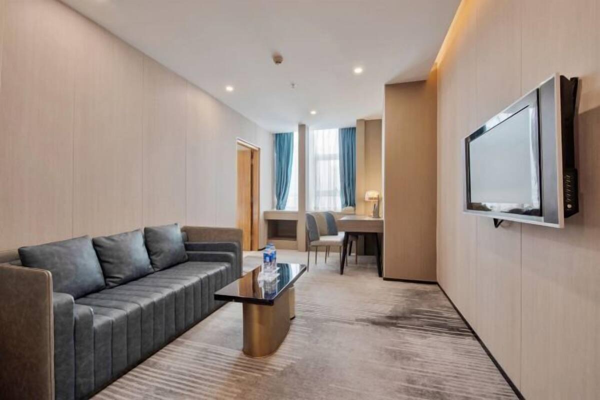 A hotel room with a sofa, a coffee table, a TV, and a desk with a chair.