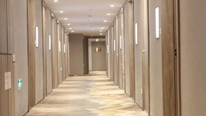 Et hotel med korridor, et mønstret gulvtæppe, indbygget belysning og døre på begge sider.
