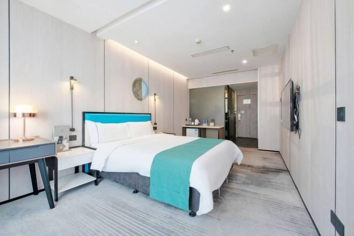 A modern hotel room with a bed, desk, and a bathroom visible through an open door.