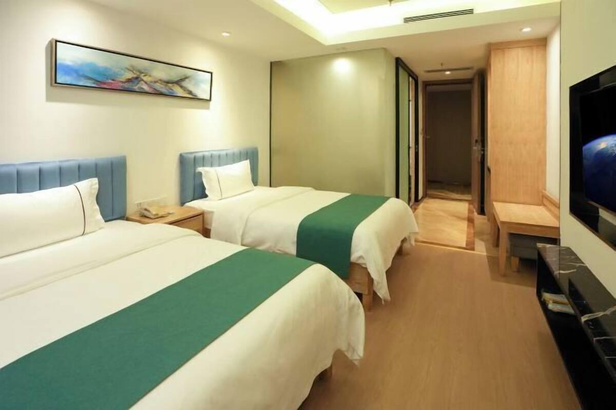 A hotel room with two beds, a TV, a painting on the wall, and a wooden floor.
