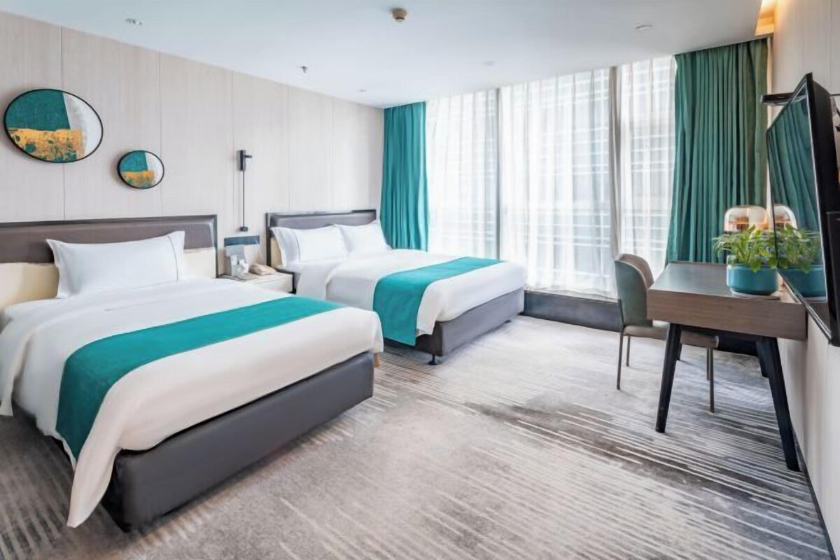 A hotel room with two beds, a desk, a chair, and a large window with curtains.