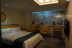 A hotel room with a bed, two yellow chairs, a small table, and a window with a view of palm trees.