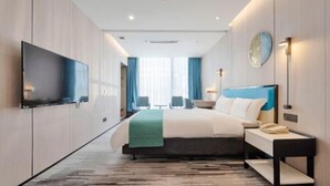 Et moderne hotelværelse med seng, sengebord, lampe og et fladskærms-tv monteret på væggen.