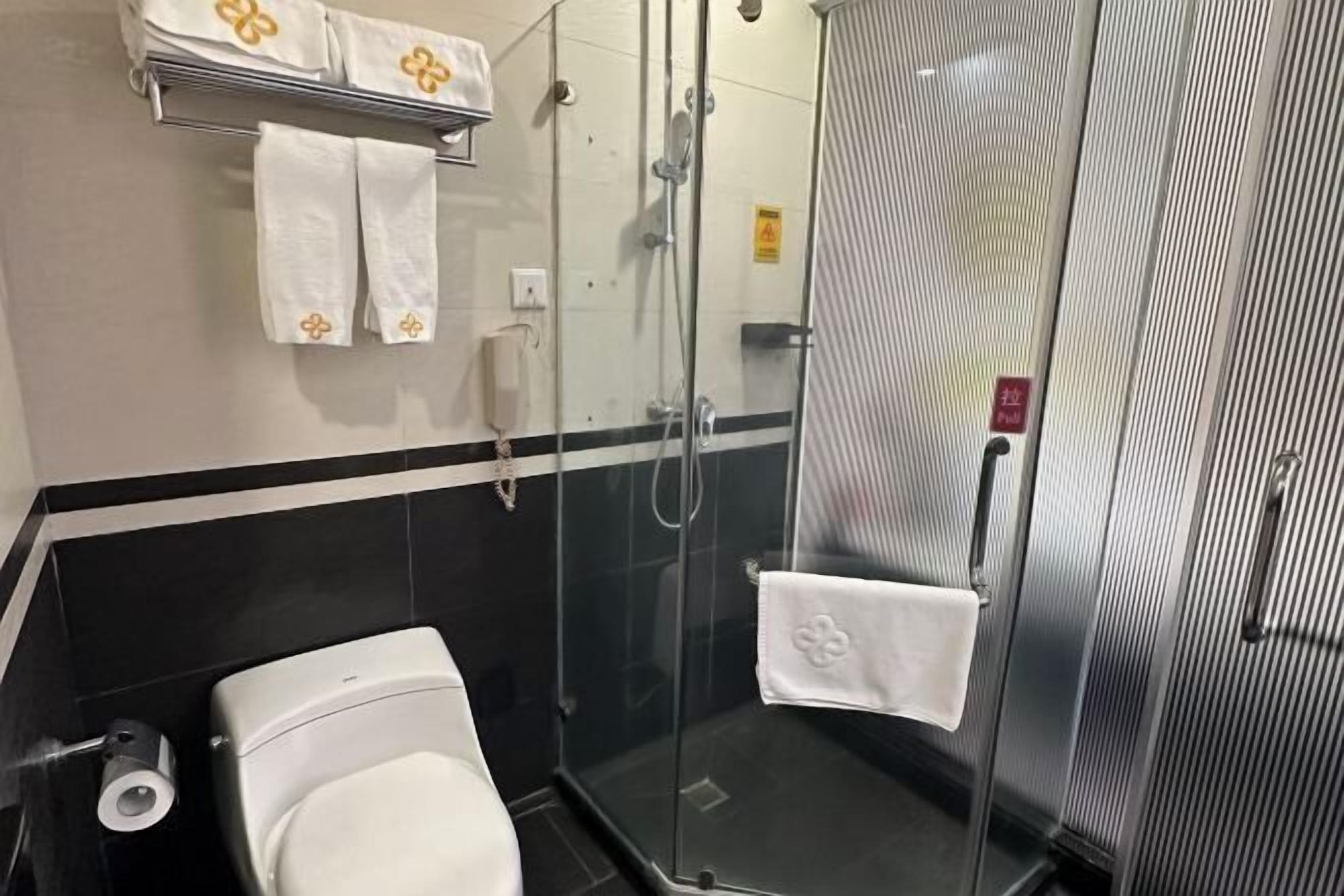A bathroom with a toilet, a glass shower enclosure, and a towel rack with white towels.