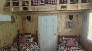 Een kamer in chaletstijl met twee houten bedden, een vide en een deur met een bordje met een berenmotief.