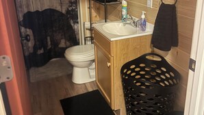 Een kleine badkamer met houten inrichting, een wit toilet, een wastafel met spiegel en een zwarte handdoekhouder.