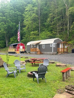 Eine rustikale Holzhütte mit Picknicktisch und Adirondack-Stühlen in bewaldeter Landschaft.