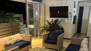 A modern lounge area with wicker furniture, a flat-screen TV, and a glass door leading to an outdoor area.