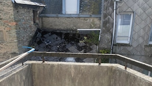 A corner of a building with a tiled floor, a concrete wall, and a metal railing. - Appartement 25 m² Avec Petite Terrasse (Cherbourg-en-Cotentin)