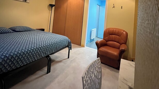 A bedroom with a bed, a chair, and a door leading to another room. - Appartement 25 m² Avec Petite Terrasse (Cherbourg-en-Cotentin)