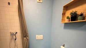 A bathroom with a shower, toilet, and a shelf with plants. - Appartement 25 m² Avec Petite Terrasse (Cherbourg-en-Cotentin)