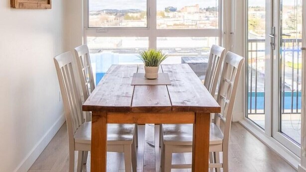 Comedor con mesa y sillas de madera, lámpara colgante y vista a una piscina a través de ventanas amplias.