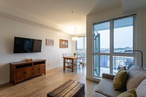 Ein modernes Wohnzimmer mit Flachbildfernseher, Holzmöbeln, einem Essbereich und einem großen Fenster mit Blick.