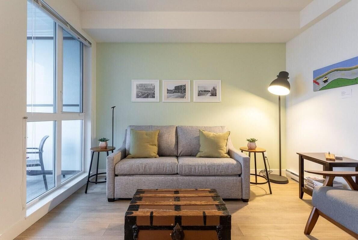 Un salon avec un canapé, une table basse, un lampadaire et une fenêtre. Trois tableaux encadrés sont accrochés au mur.
