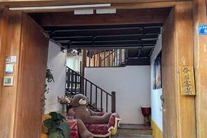 Interior de madera con una escalera, un gran oso de peluche en un asiento estampado en rojo y blanco, y un cartel con caracteres chinos.