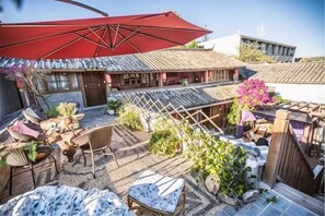 An outdoor patio with a red umbrella, wicker furniture, and potted plants. - Lijiang Time Jinghao Bieyuan Inn (Lijiang)