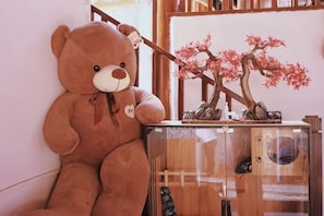 A large brown teddy bear sitting on a wooden table next to a glass display case with a bonsai tree. - Lijiang Time Jinghao Bieyuan Inn (Lijiang)