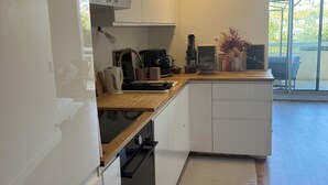 Eine moderne Küche mit weißen Schränken, einer Holz Arbeitsplatte und einem eingebauten Ofen. Auf der Arbeitsplatte stehen eine Kaffeemaschine, ein Wasserkocher und eine kleine Pflanze.