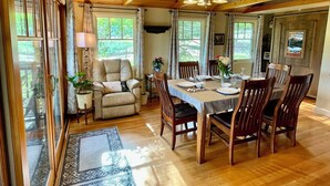 Un coin repas avec une table en bois, dressée pour quatre personnes et entourée de chaises, offrant une vue sur la verdure à l’extérieur.