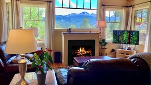 Un salon chaleureux avec une cheminée, des canapés en cuir, un téléviseur et une vue sur les montagnes grâce à de grandes fenêtres.
