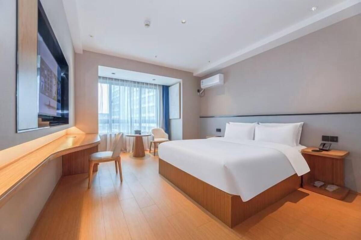 Een moderne hotelkamer met een groot bed, een bureau, een stoel en een raam met gordijnen.